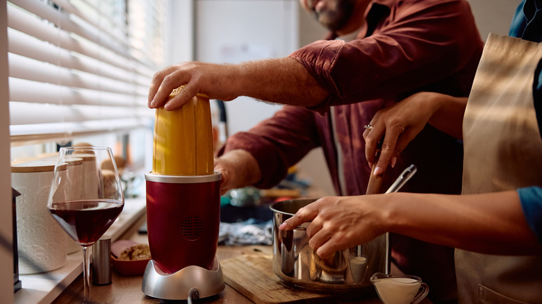 Soup being blended in a blender next to a glass of wine and a pot