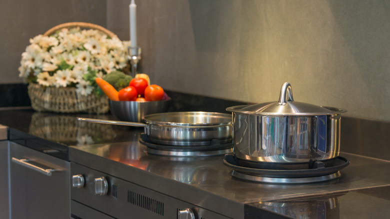 Stainless steel pot and pan on a burner next to fruit and flowers