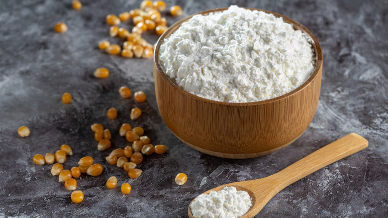 Cornstarch in a bowl and on a wooden spoon with corn kernels surrounding them