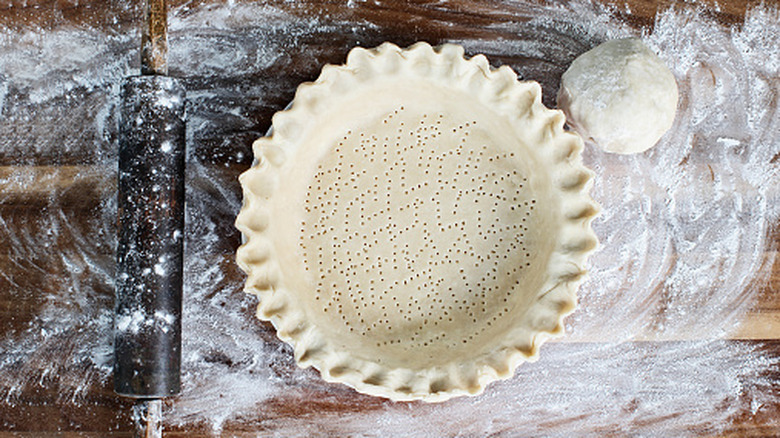 Raw pie crust ready to be blind baked on  table strewn with flour