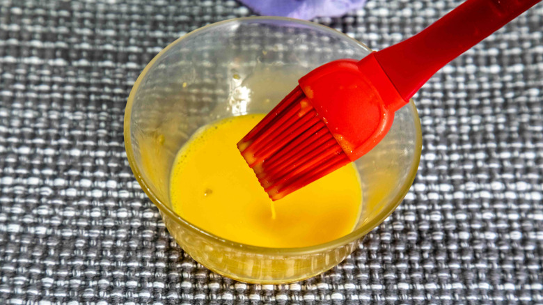 Close up of a bowl of egg wash with a red silicone brush