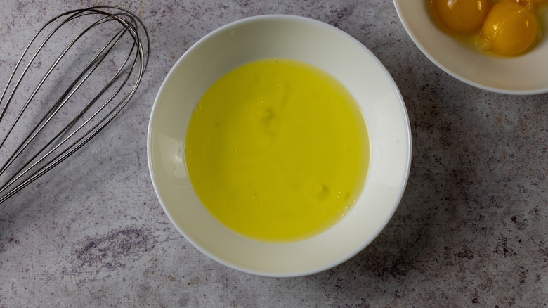 Egg whites and egg yolks in bowls next to a whisk