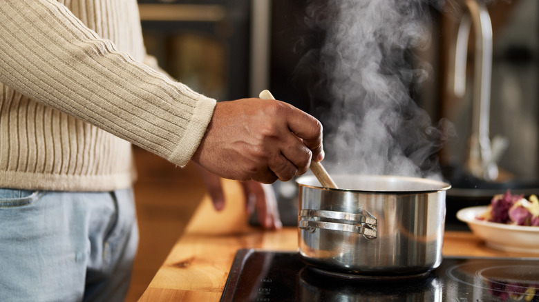 Person stirring a pot on the stove using a wooden spoon