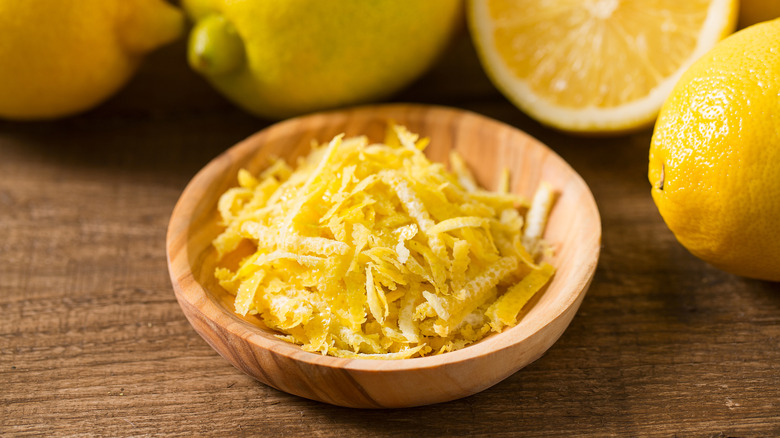 A small wooden bowl with fresh lemon zest against a background with several lemons