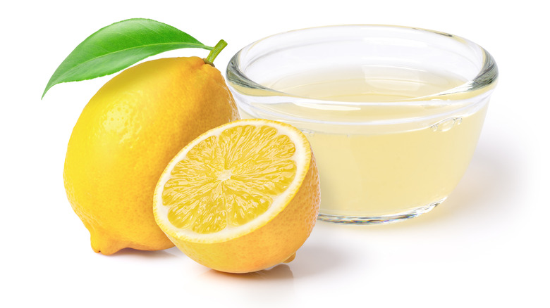 A lemon and a half lemon next to a bowl of fresh lemon juice