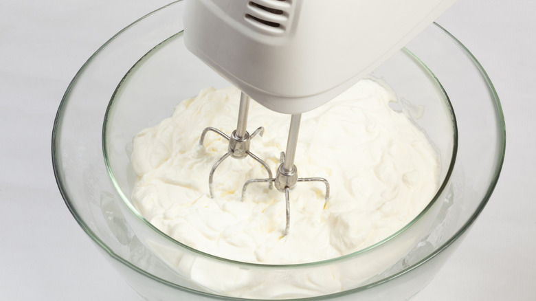 A bowl full of whipped cream inside a bowl filled with ice, along with a hand mixer