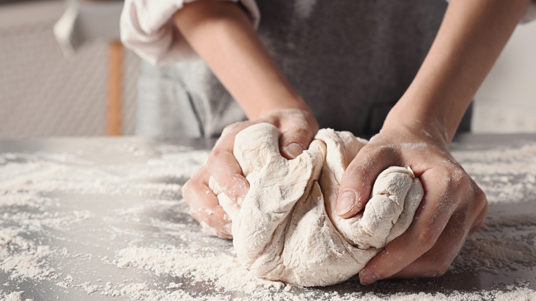 A baker kneading a flour-dusted ball of dough on a table