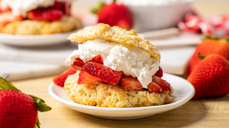 Strawberry shortcake on a white plate with fresh strawberries on the side