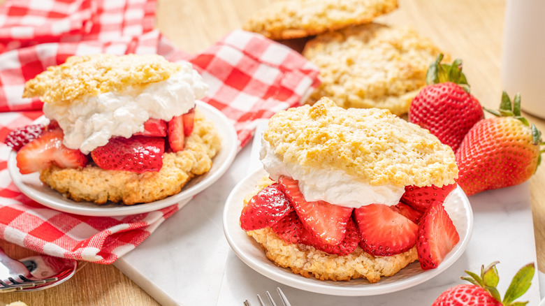 A plate of strawberry shortcakes on a table with fresh strawberries on the side
