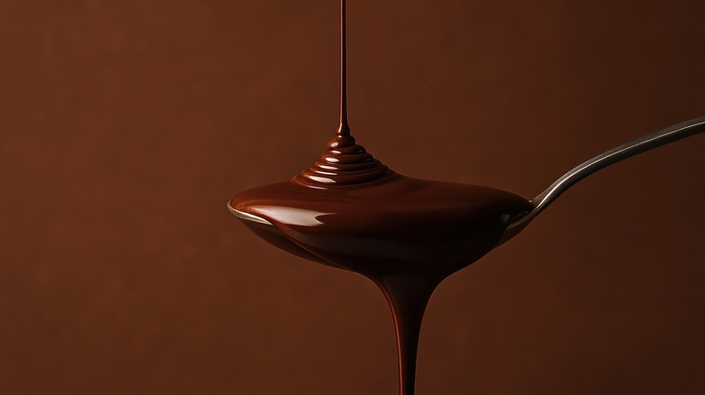 Chocolate sauce drizzling on spoon with brown background