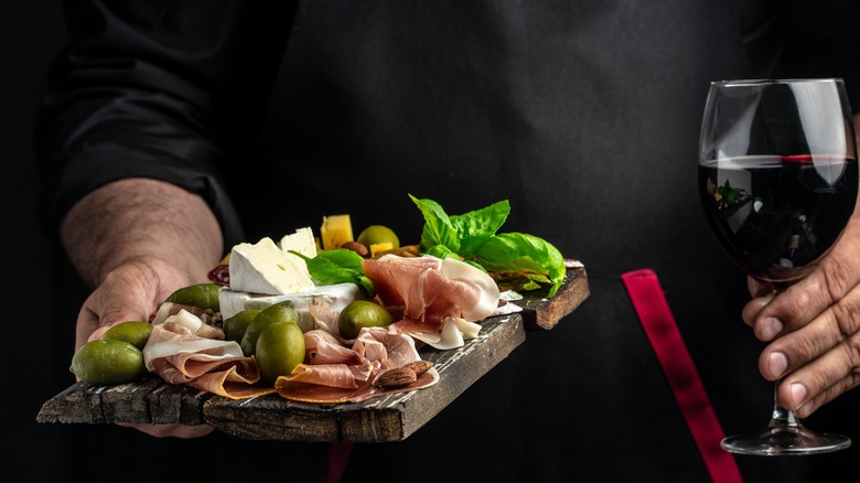 Someone holding wine and a charcuterie board