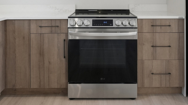 Close up of a modern stove set into wooden cabinets with white marble countertop