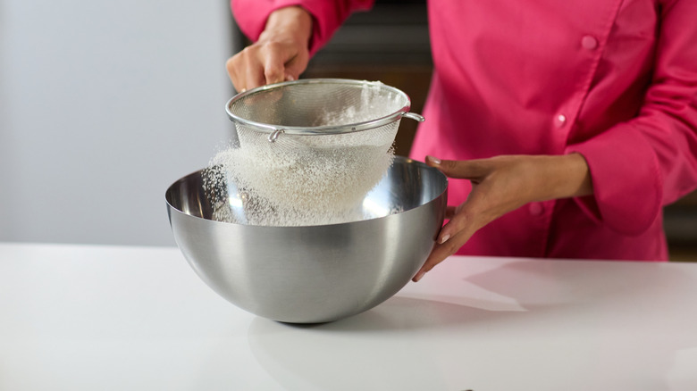 A person sifts dry ingredients into a metal bowl