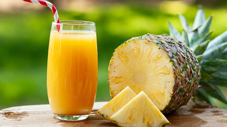 A glass of pineapple juice with a straw sits next to a whole pineapple that's been sliced open on the bottom