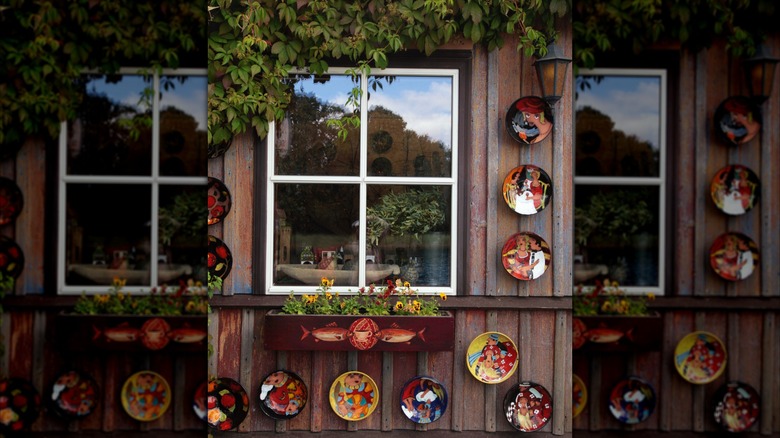 A rustic square window surrounded by colorful, wall-mounted plates, flowers, and other plants