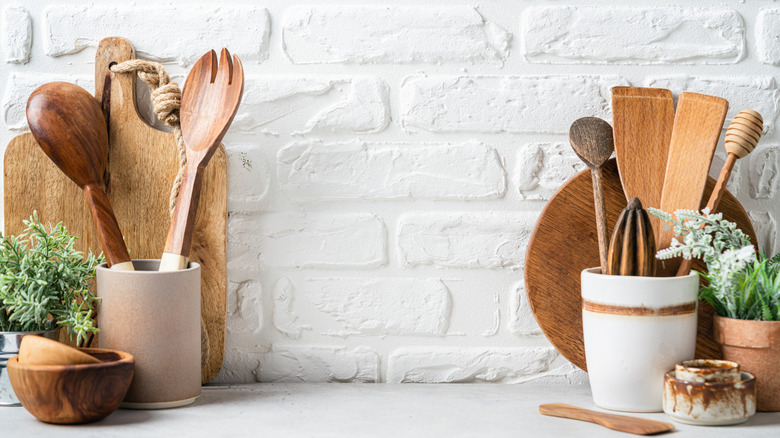 Two crocks full of kitchen utensils, with two wooden cutting boards behind them against a white wall
