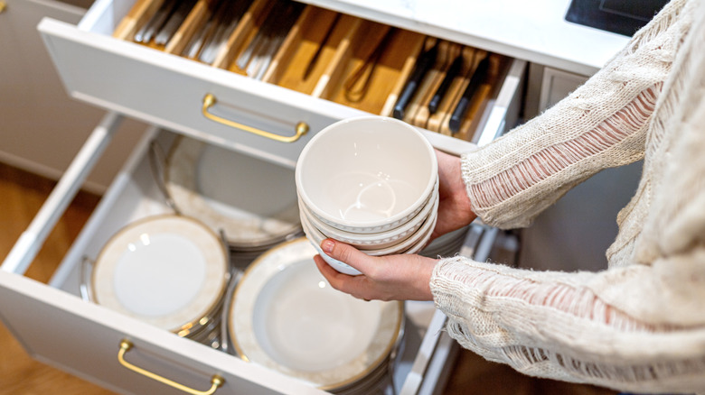 A woman holds bowls over well-organized drawers