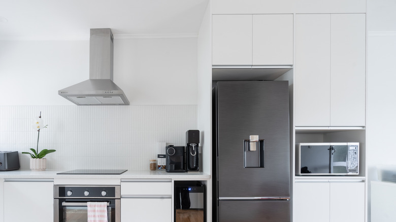 A kitchen with a modern refrigerator, with a cupboard above it