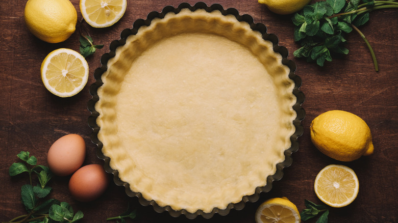 Pastry tin lined with pastry and surrounded by lemons and eggs