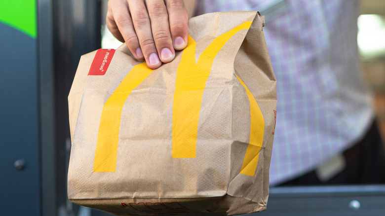 McDonald's employee passing a to-go bag through the drive-thru window