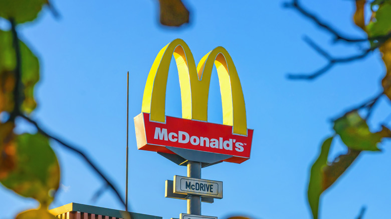 A tall McDonald's sign seen through green tree leaves