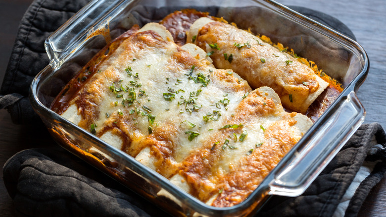 Baked enchiladas in a glass baking dish on dark oven mitts.