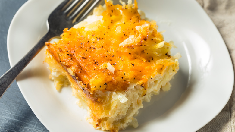 Serving of potato casserole on white plate with fork.