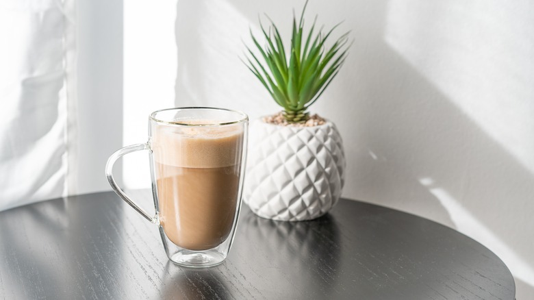 creamy cup of coffee with milk on table next to plant