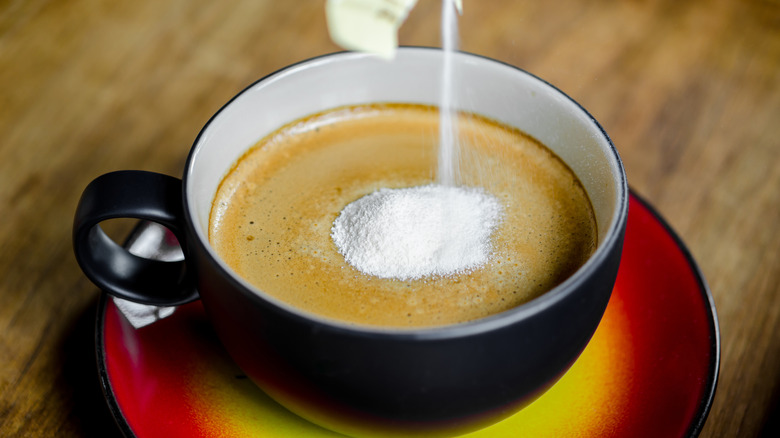 Powdered milk being poured into a cup of coffee