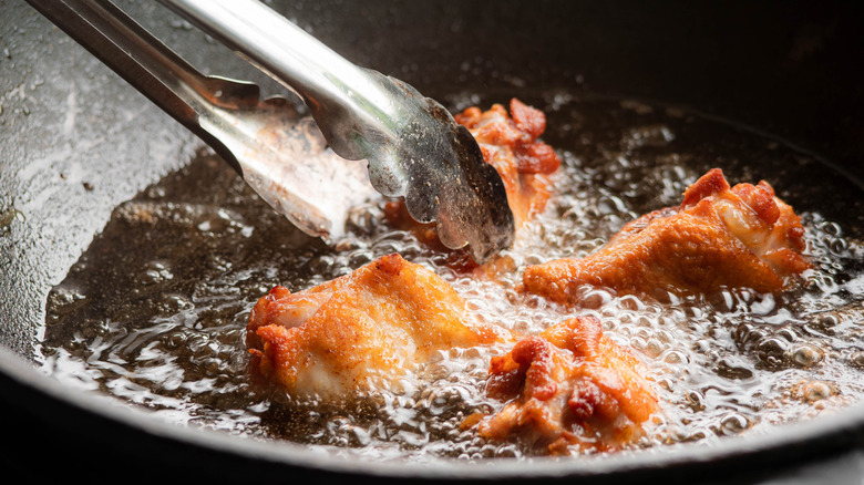 Tongs touching frying chicken