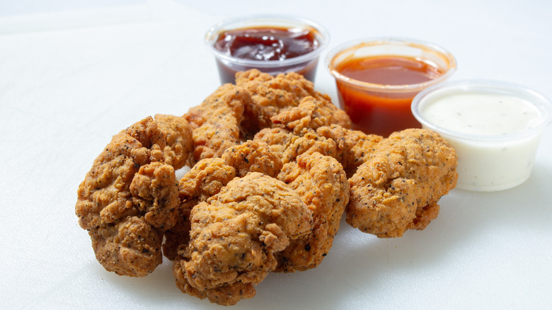 Boneless wings on a white table with three cups of dipping sauces on the side