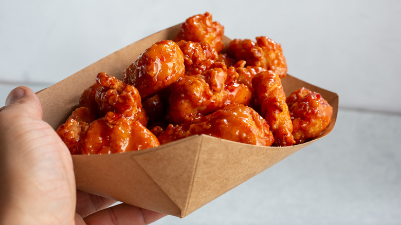 A person holding a paper tray full of boneless chicken wings