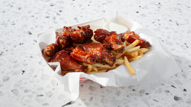 Chicken wings along with French fries in a white container placed on a white table