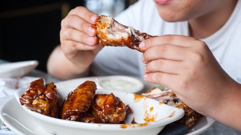A person eating chicken wings from a white plate