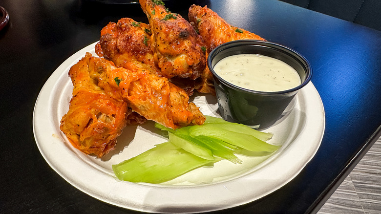 Buffalo wings with a dip and celery on the side on a white plate