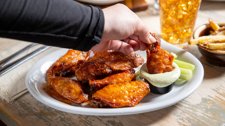 A woman dipping a chicken wing into sauce from a full plate of wings