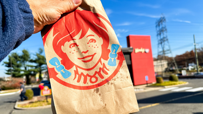 Brown paper Wendy's takeout bag, held up in front of a drive-through restaurant.