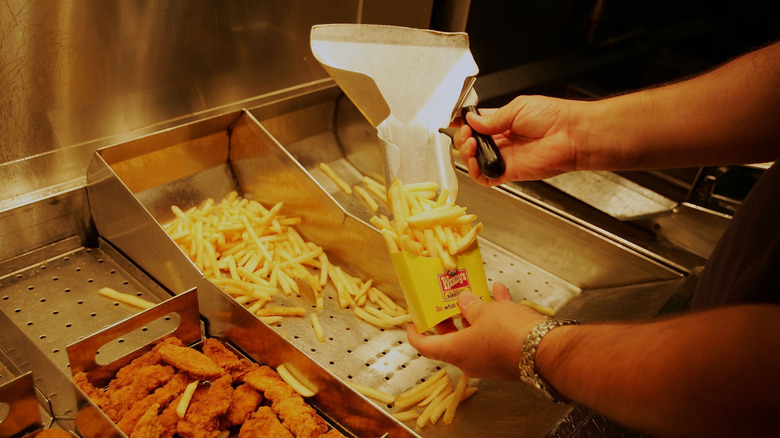 A Wendy's employee scoops fries off the line to pour into a serving container.