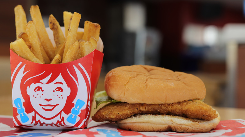 A chicken sandwich with only lettuce visible as a topping next to an order of Wendy's fries.