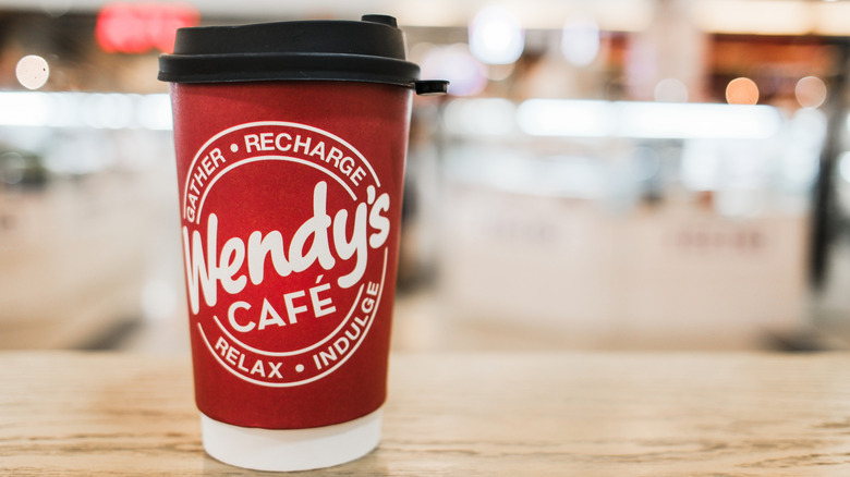 A red Wendy's coffee cup against a blurred background.