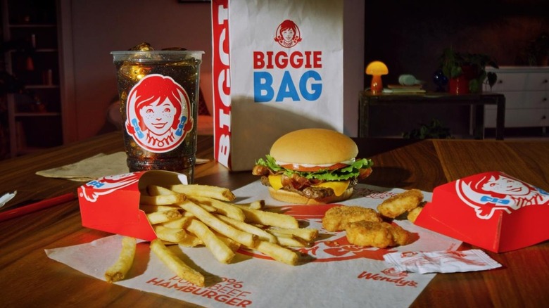 A Jr. Bacon Cheeseburger, chicken nuggets, fries, and soda spread on a table in front of a Biggie Bag.