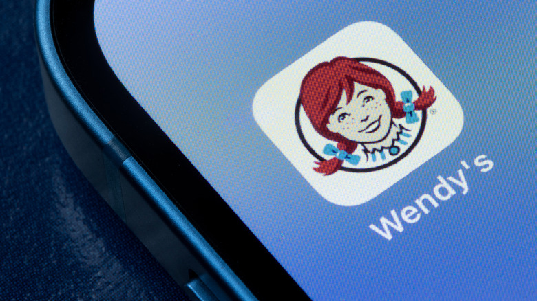 The Wendy's app logo on the screen of a smartphone against a blue background.