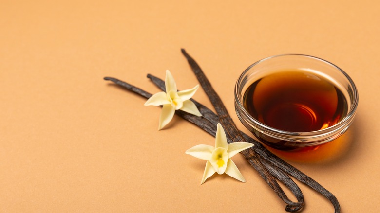 Vanilla extract in bowl, with vanilla pods and flowers