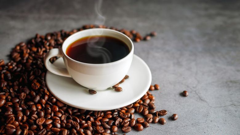 A steaming cup of coffee surrounded by coffee beans