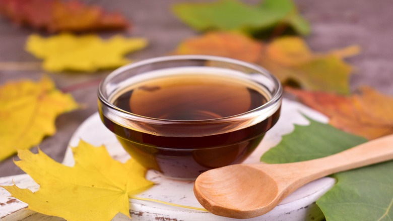 Small glass bowl of maple syrup, surrounded by maple leaves