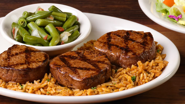Filet Medallions on a bed of rice with a bowl of green beans on a white plate