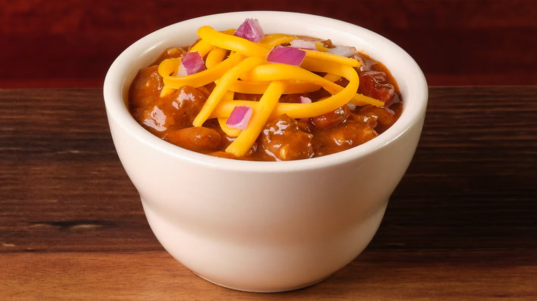 A white bowl of Texas Roadhouse chili topped with cheese and onion