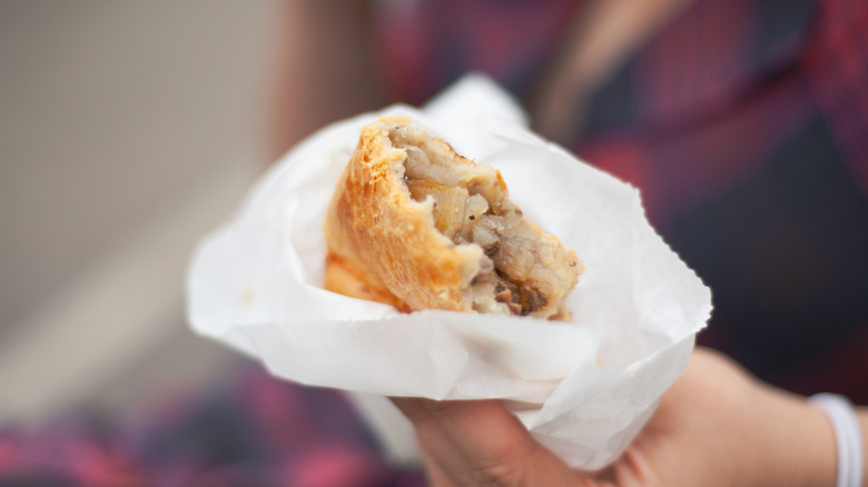 Person holding a Cornish pasty wrapped in butcher paper