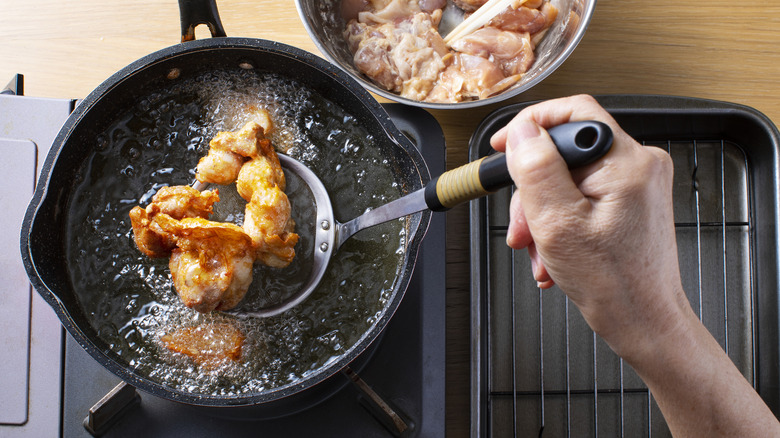 A hand with a tool pulling deep-fried chicken out of a pan