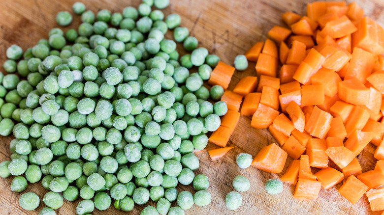 Pile of frozen peas next to pile of freshly chopped carrots
